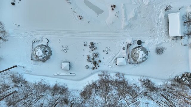 Top-down aerial of geodesic glamping domes in snowy forest near Riga, Latvia, revealing modern eco tourism accommodation and abstract winter landscape patterns.