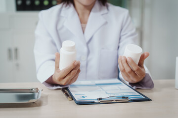 Doctor in white coat holding two medicine bottles over clipboard on desk in clinic, comparing prescription options, healthcare consultation concept.