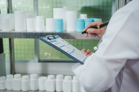 Pharmacist or lab technician in white coat checking inventory and paperwork on clipboard beside shelves of medicine bottles in a clean modern pharmacy or lab.