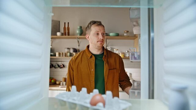 Hungry guy open empty refrigerator searching food standing home kitchen closeup.