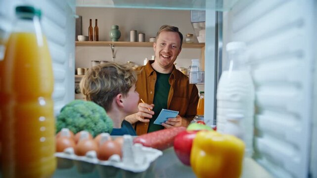 Refrigerator view father son looking shelves making shopping list home closeup.