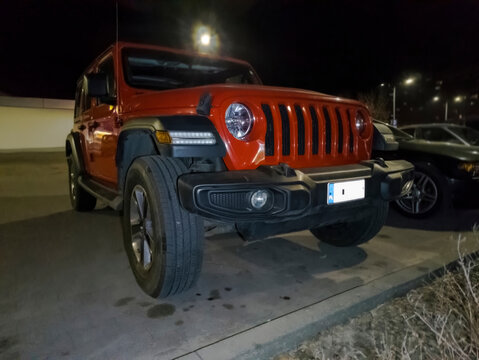 Polska, Ostrowiec Świętokrzyski, 13 marca 2026, 20:24. Czerwony Jeep Wrangler Sport &ndash; amerykański klasyk off-roadowy nocą. Pojazd wyr&oacute;żnia się  okrągłymi reflektorami, siedmioszczelinowym grillem