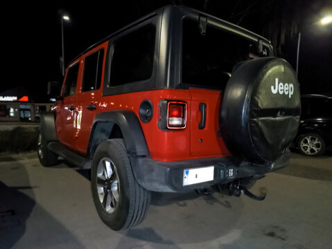 Polska, Ostrowiec Świętokrzyski, 13 marca 2026, 20:24. Jeep Wrangler &ndash; czerwony, klasyczny samoch&oacute;d terenowy nocą na parkingu. Pojazd to klasyczny samoch&oacute;d terenowy z widocznym kołem zapasowym 