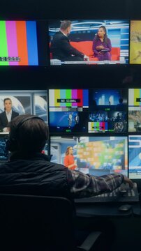 Vertical Screen. Backstage Tv Station Production Control Room With Male Operator Managing Live News Broadcasting, Switching Channel Feeds and Monitoring Anchor Segments Across Studio Screens.