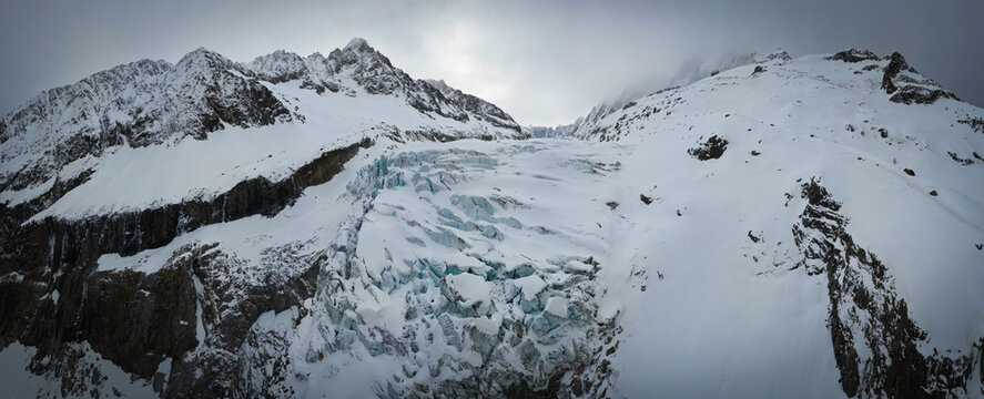Panoramic aerial view of the formidable Glacier d'Argentiere, a frozen river of blue ice snaking through snow-dusted peaks under a brooding sky, Chamonix, Auvergne-Rhone-Alpes, France.