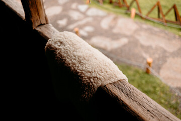 Natural sheepskin fur resting on a wooden railing outdoors. Rustic cozy decor element in a rural mountain setting with soft natural light. © ShvedKristina