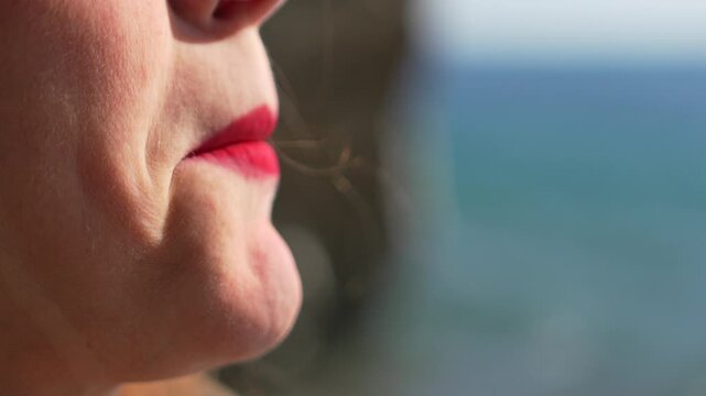 Lipstick Makeup Beauty woman applying bright red lipstick to her lips with a blurry ocean background on a sunny day