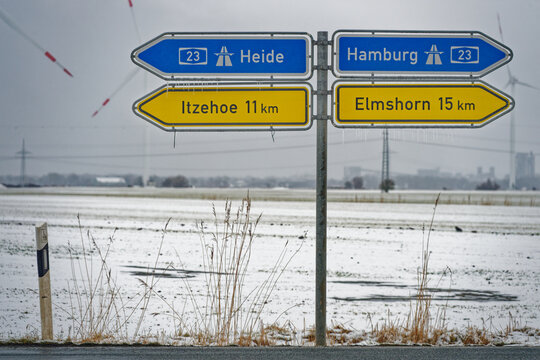 Winter road signs showing directions to Heide Hamburg Itzehoe and Elmshorn in snowy landscape