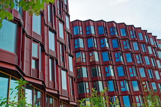 Modern red building facade with large blue reflective windows and green foliage