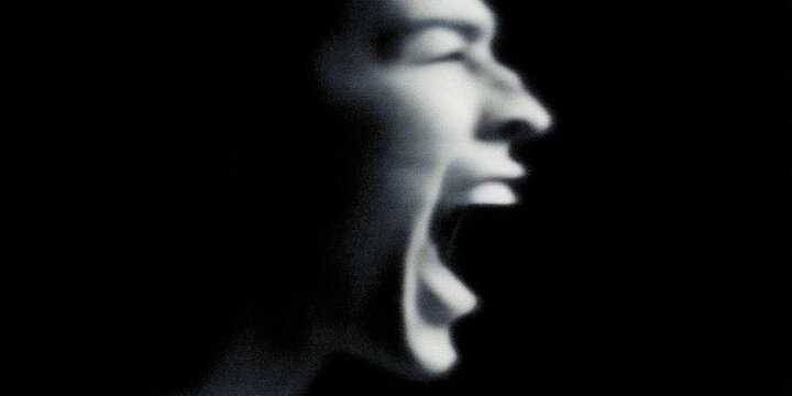 A powerful portrait of a man's face, captured in high contrast, depicts a moment of intense emotion, perhaps fear, rage, or extreme excitement. The man's face is contorted in a scream