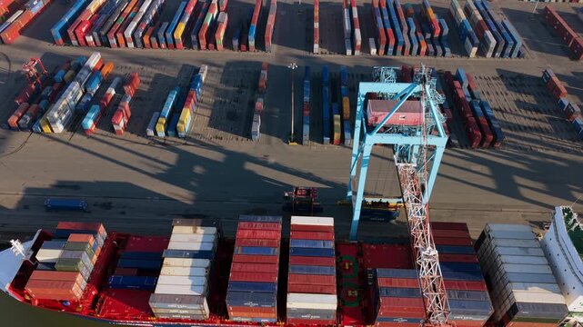 Aerial video of a container vessel docked at Seaforth terminal, showing a blue gantry crane in operation and rows of shipping containers casting long morning shadows.