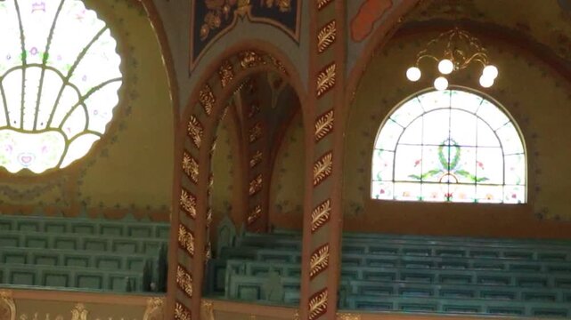 Cinematic low angle view of ornate balcony and glowing chandelier in historic synagogue