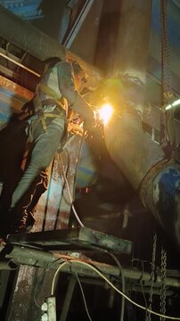 Industrial welder welding coal discharge pipe at height at power plant.