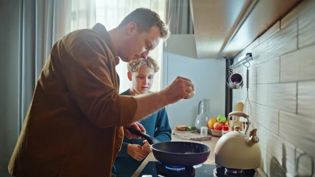 Son helping dad frying breakfast omelette at kitchen stove closeup. Caring man