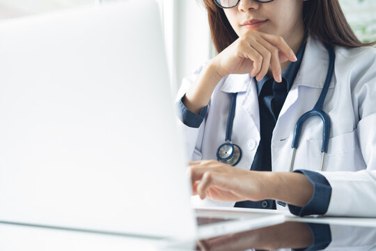 Female doctor working at laptop in hospital office, using medical online service, application for telemedicine service with patient or online meeting, web conference