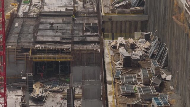 Worker cleaning steel rebars with water before concrete pouring at the site. Foundation construction, industrial building forms, and site preparation process.