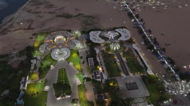 Drone shot above Marina Beach at night, capturing glowing lights on the white memorial structures of MGR, gentle ocean waves, and the busy beachfront road running parallel to Chennai&rsquo;s coastline.