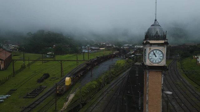 Atmospheric aerial footage of iconic clock tower in misty Paranapiacaba historic district, Santo Andr&eacute;, S&atilde;o Paulo. Low clouds roll over railway town, creating moody ambiance.