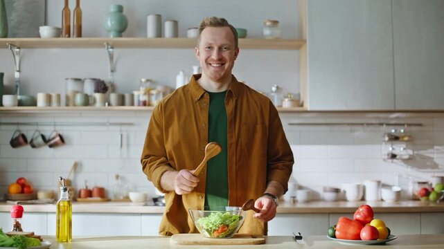 Cheerful man sniffing salad enjoying vegetable aroma standing kitchen closeup.