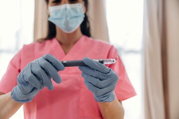 Healthcare professional in pink scrubs wearing gloves and a mask holds an insulin pen for diabetes management in a well-lit medical environment