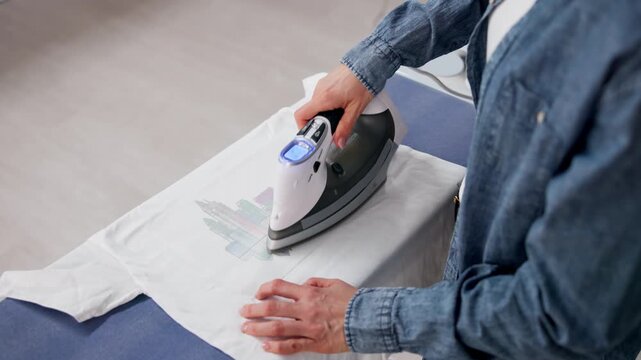 Woman Using Iron-On Heat Transfer To Apply Custom Design On T-Shirt