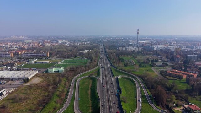 Aerial top view of major highway interchange on A50 Tangenziale Ovest Milan with flowing traffic. On horizon visible Torre Telecom di Rozzano, urban infrastructure and mobility concept.