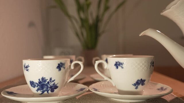 Pouring fresh hot water from a white porcelain teapot into an elegant vintage ceramic tea cup with blue floral patterns, cozy home atmosphere, slow motion.