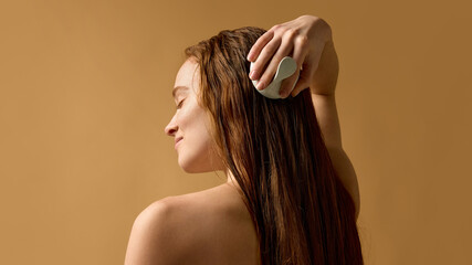Woman massaging scalp with brush on wet hair in studio. Concept of scalp stimulation, care routine,...