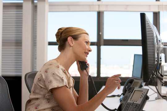 Side view of a Businesswoman in an office sitting at her desk talking on the phone