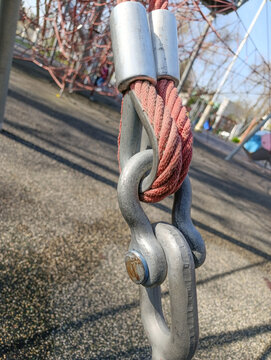 Steel chain link and shackle with red rope attachment close-up, outdoor rigging connection detail.