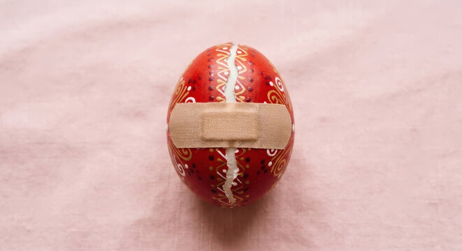 Broken Easter egg with adhesive bandage on a pink background, conceptual image of fragility and healing, generative AI