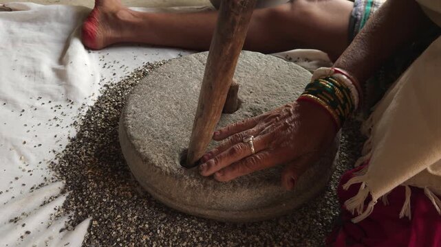 Close-up of a Indian woman using a traditional stone grinder to process grains or spices by hand. This authentic rural scene highlights Indian culture, handmade food preparation