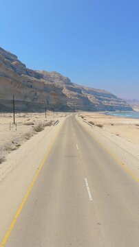 Aerial view of a young man in traditional Omani clothing walking along a remote coastal highway with massive desert cliffs, Salalah, Oman.