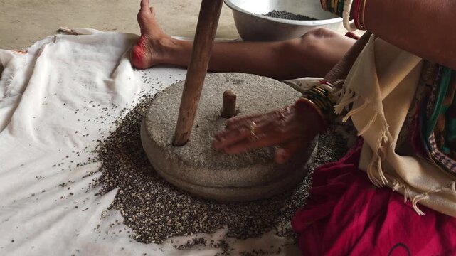 Close-up of a Indian woman using a traditional stone grinder to process grains or spices by hand. This authentic rural scene highlights Indian culture, handmade food preparation