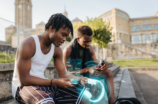 Two young men reviewing fitness data on smartphones after urban basketball practice
