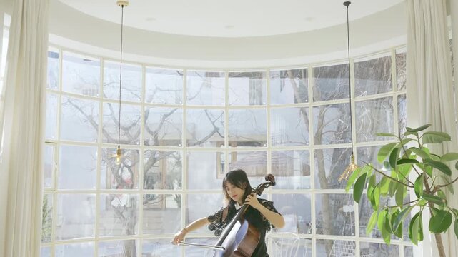 Beautiful young woman musician cellist rehearsal and performance of cello in concert hall classical music orchestral instrument string, focused on strings, bow movement, musical expression
