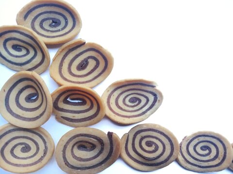 "Kuping Gajah'" is a traditional Indonesian snack that is round, thin, wide, and slightly concave, resembling an elephant's ear with a distinctive spiral pattern, brown and white in color, with a very