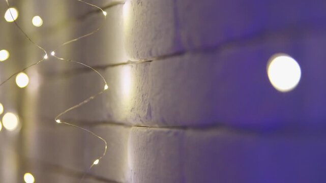 Flickering warm white garland lights hanging on textured white brick wall with soft bokeh glowing