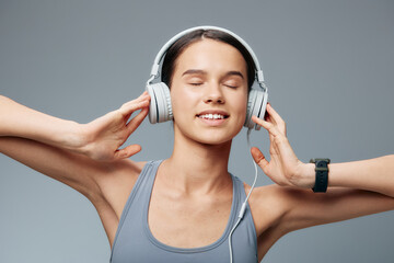 Fototapeta premium Woman fitness enthusiast wearing headphones, enjoying music during workout in a studio. Relaxed pose with eyes closed, athletic tank top, calm energy and focus.