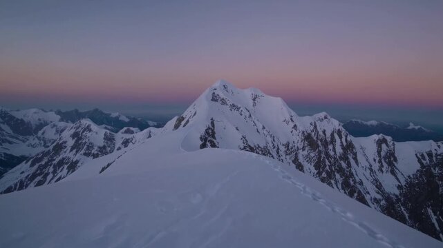 Snowy summit at pastel twilight with soft horizon hues, pristine cornices and sweeping ridge lines calm dawn expedition atmosphere for mountaineering, photography and early ascent planning.