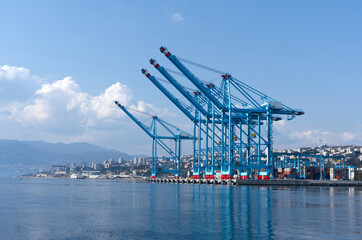 Obraz premium Large commercial port with blue container cranes on waterfront — global shipping logistics, maritime infrastructure, cargo terminal aerial view