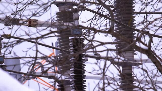 Close view of icy substation insulators and steel structures in freezing winter weather with blurred branches and white sky.