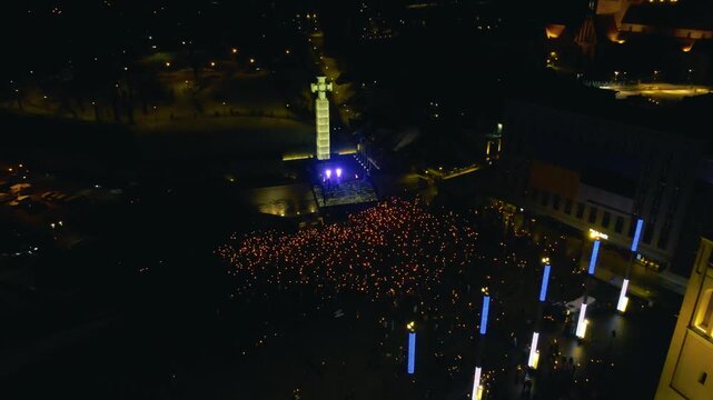 Aerial night view of a torchlight crowd gathering at Tallinn Freedom Square beside the illuminated War of Independence monument during Estonian Independence Day.