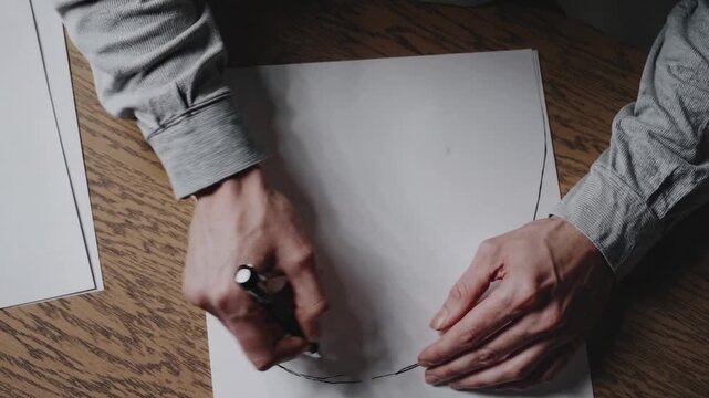 white hands sketching circle on paper wooden desk felttip pen careful tracing focused motion product designer mapping logo curve ambient daylight minimal composition tactile process precise wrist