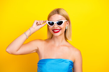 Fototapeta premium Young chic stylish woman in blue strapless dress wearing white sunglass against a bright yellow background