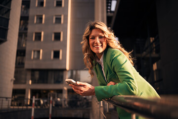Fototapeta premium Businesswoman holding smartphone smiling in urban city