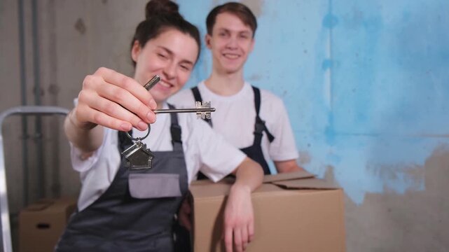 Own home. Mortgage relocation concept. Happy couple holding key from new first house. Family celebrating moving day. Husband wife customers buyers purchase real estate hold moving box showing keys
