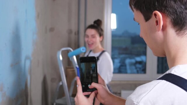 Couple in new home. Man taking photo woman during repair works painting walls. Happy family bloggers painting wall make selfie in social network. Happy family doing home renovation. DIY renew home