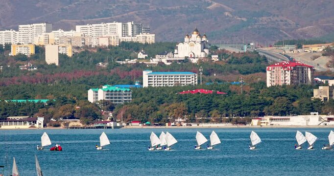 Gelendzhik resort. Gelendzhik Bay. Sailing regatta. A group of sailboats are sailing in the ocean near a city. The sailboats are of different sizes and are spread out across the water. The scene is pe