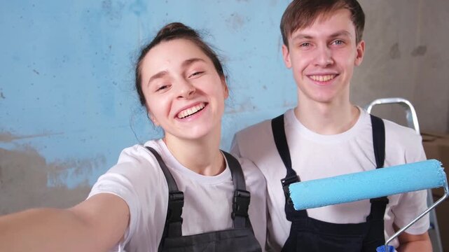 Couple in new home having video call during repair works painting wall together. Happy family bloggers painting wall in new house streaming chatting in social network. Home renovation DIY renew home
